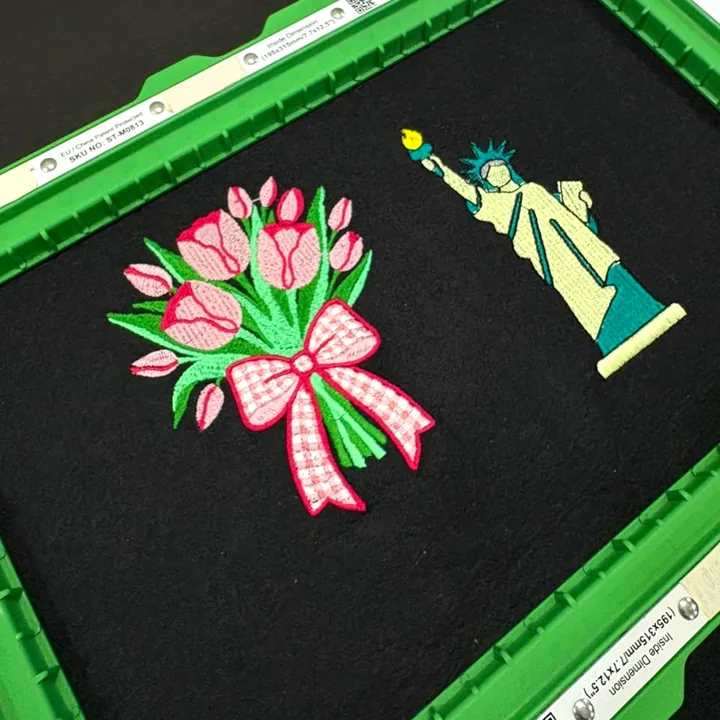 A tulip bouquet and a Statue of Liberty embroidered on black fabric, still in a green magnetic hoop